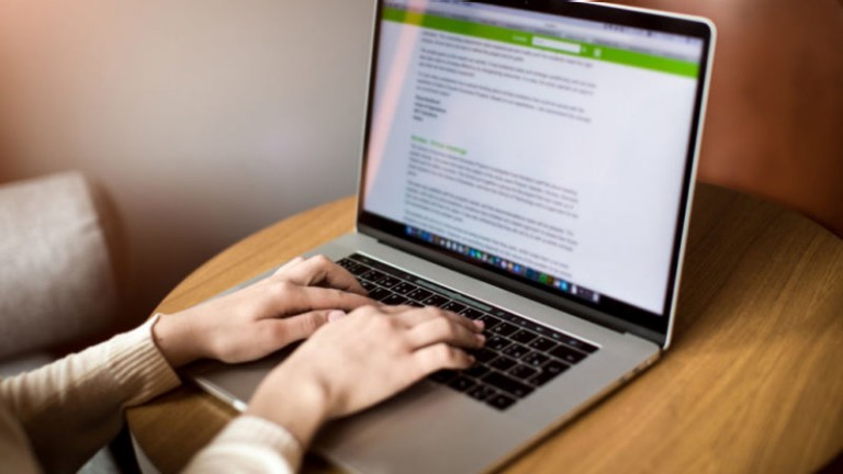 Writer keyboarding promotional text on laptop computer while sitting in coworking space