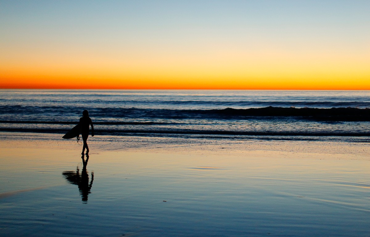 A lone surfer heads home after surfing past sunset in Leucadia, CA