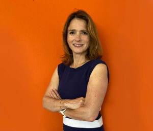 Janice smiling for a photo with her arms crossed in front of an orange background.