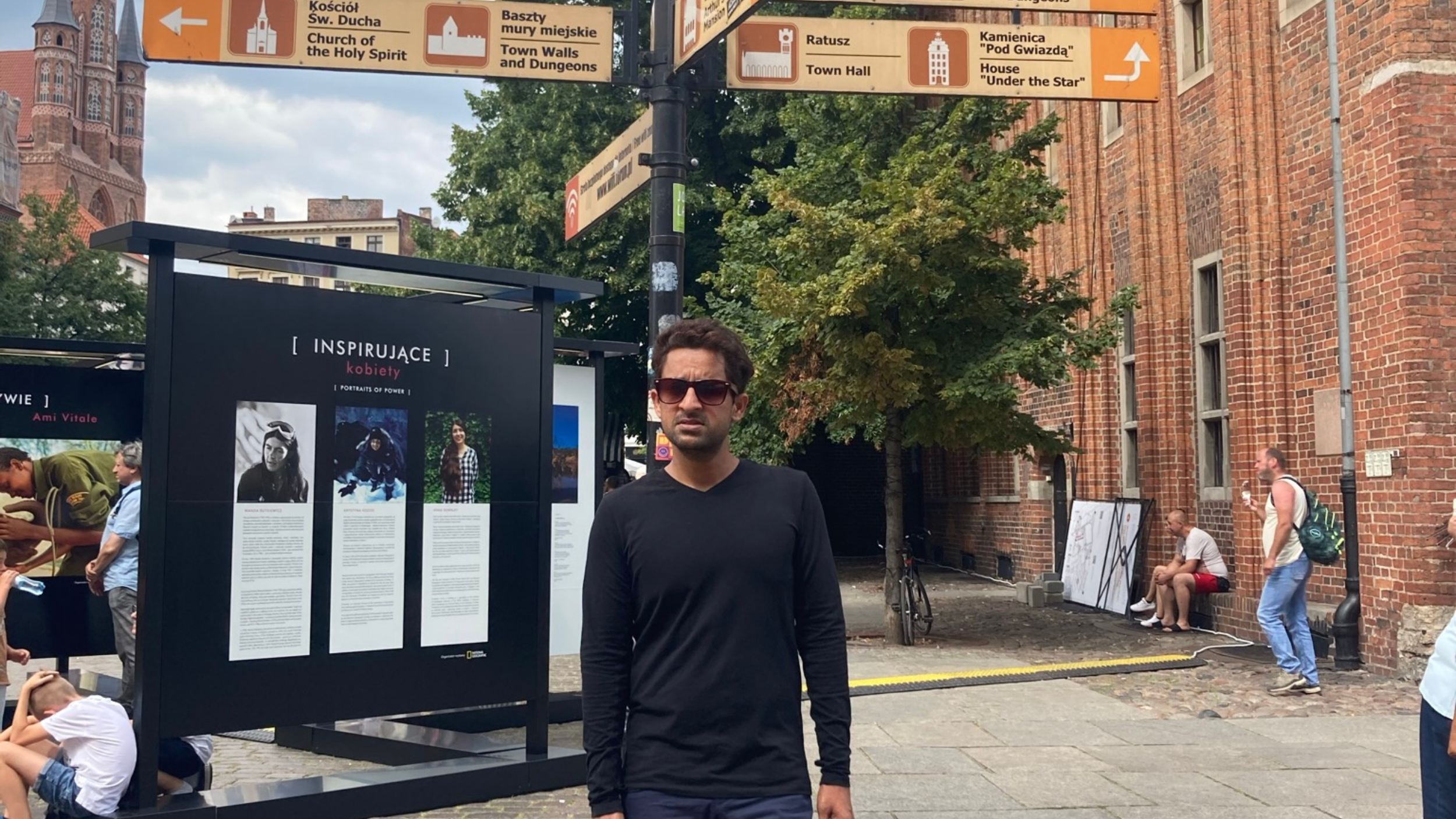 Srikant, wearing a dark shirt and sunglasses, standing in front of a street sign in Gdansk.