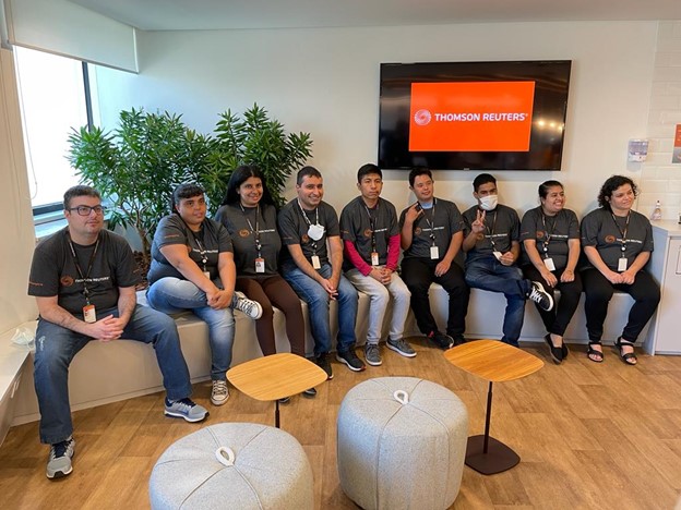 Nine people sitting beside each other inside an office, all wearing Thomson Reuters shirts.