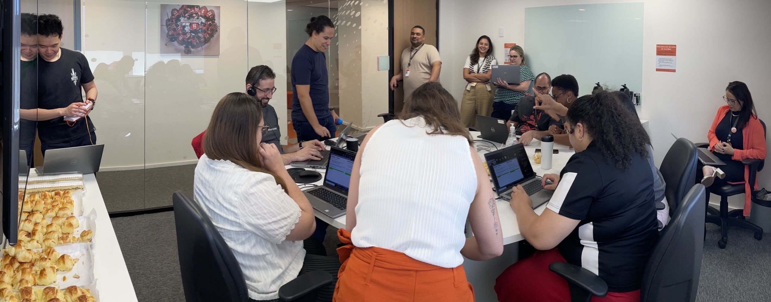 A group of teammates sit and stand around a desk looking at their laptops and talking to each other during the Global AI Hackathon.
