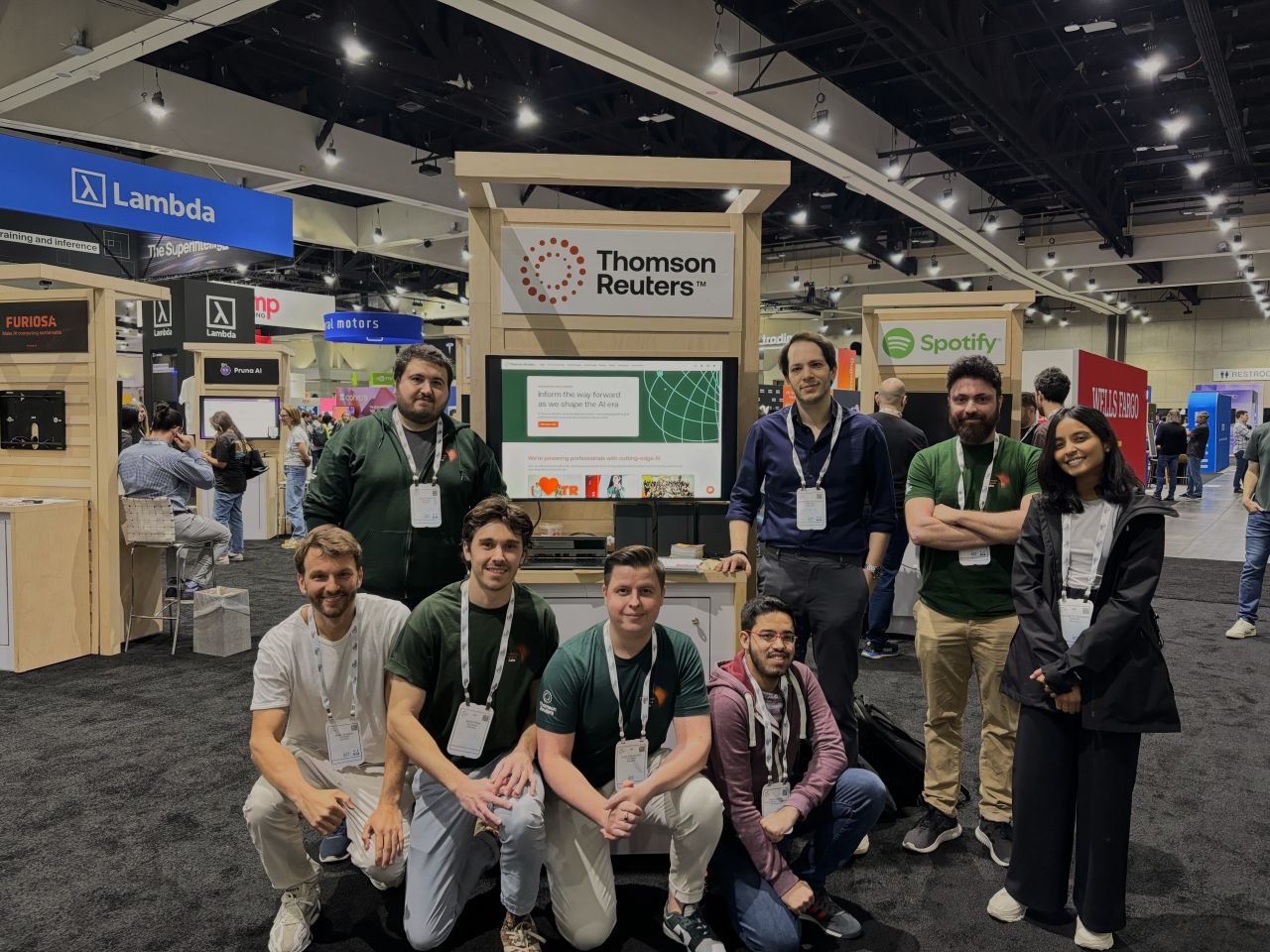 A group of individuals at a conference posing for a photo in front of a Thomson Reuters booth