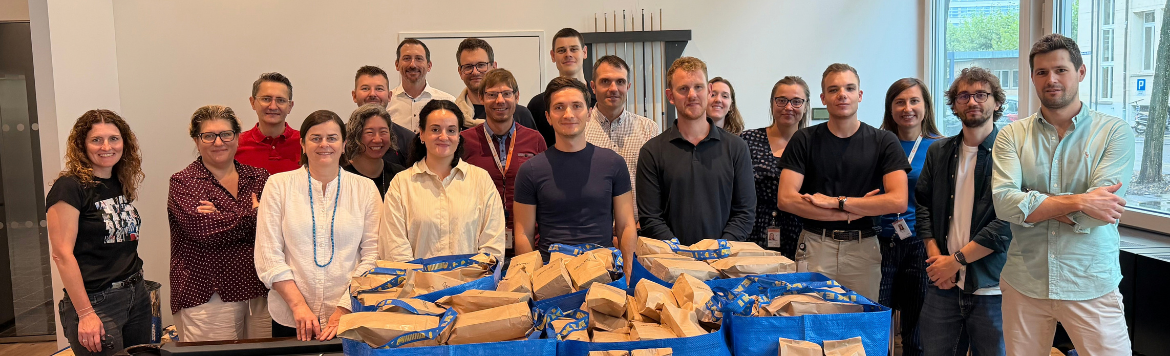 Thomson Reuters employee team of 20+ people standing together in an office with city skyline views, gathered around donation boxes during a team volunteering event