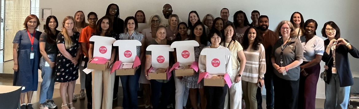 Diverse group of 25+ Thomson Reuters employees standing together, many holding white and pink HOPE-branded boxes during a charitable giving and volunteering initiative